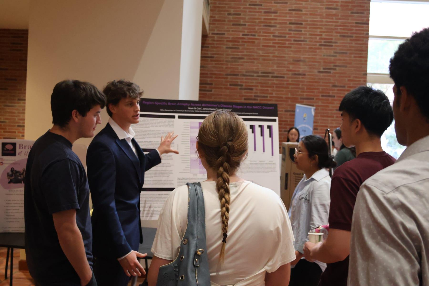 A Neurowave member presents a research poster on Alzheimer's disease to a group of students.